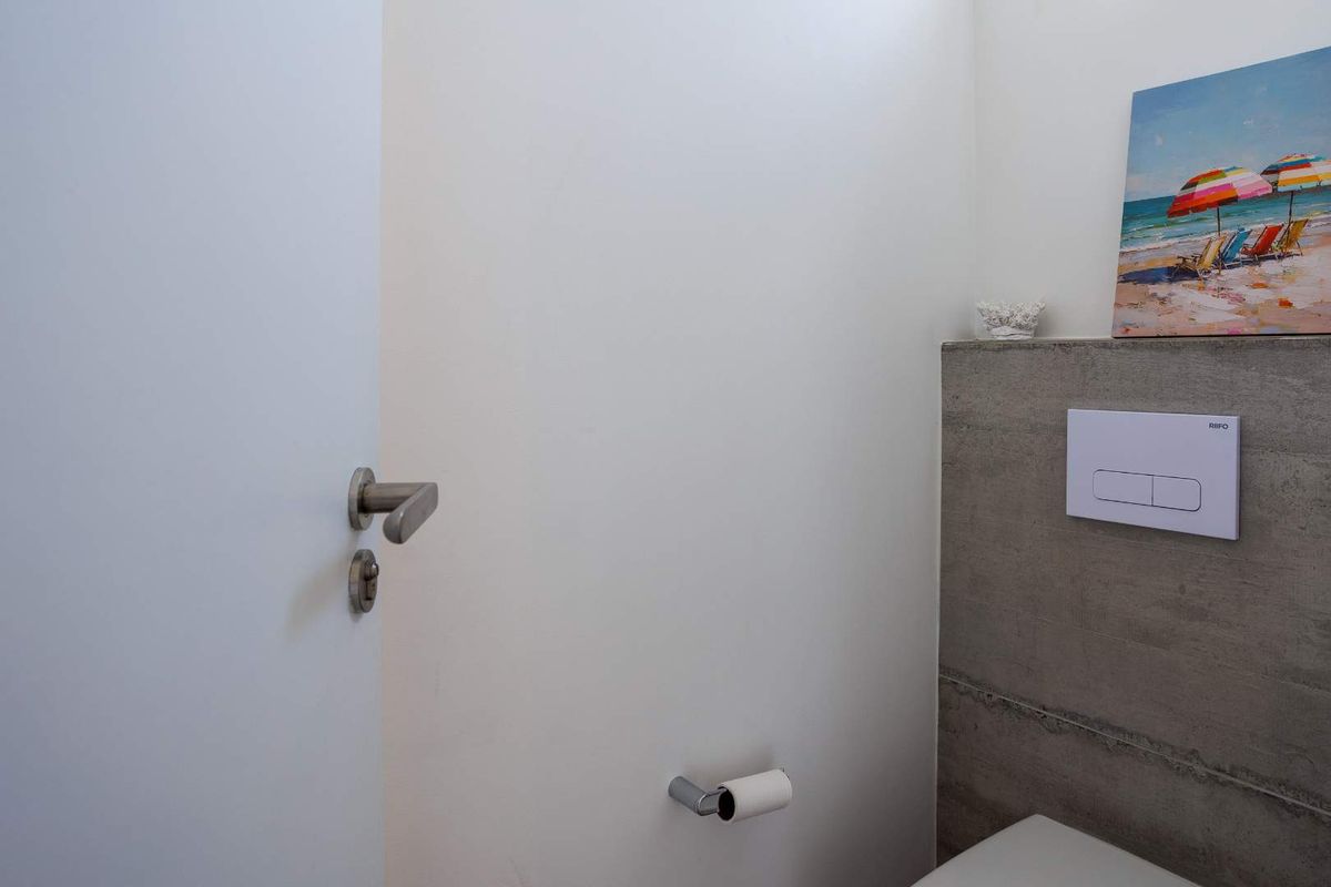 A modern bathroom featuring a minimalist wall-mounted toilet flush plate and a contemporary exposed concrete feature wall.