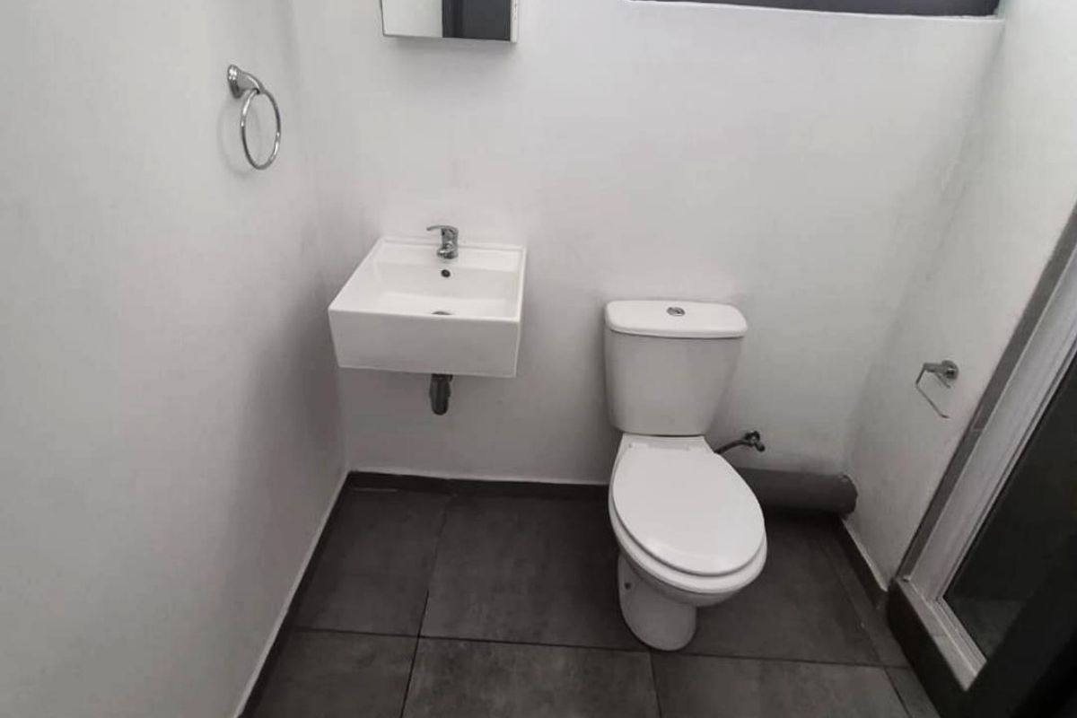 A compact, modern bathroom featuring a wall-mounted basin, a standard toilet, and dark floor tiles, presenting a clean and functional space.