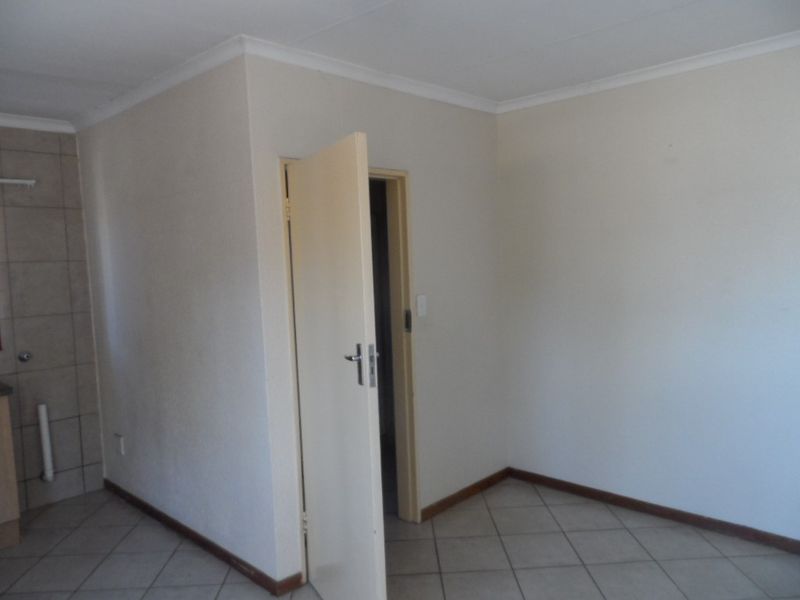 An empty living area featuring neutral walls, tiled flooring, and coved ceiling details, providing a blank canvas for interior design.