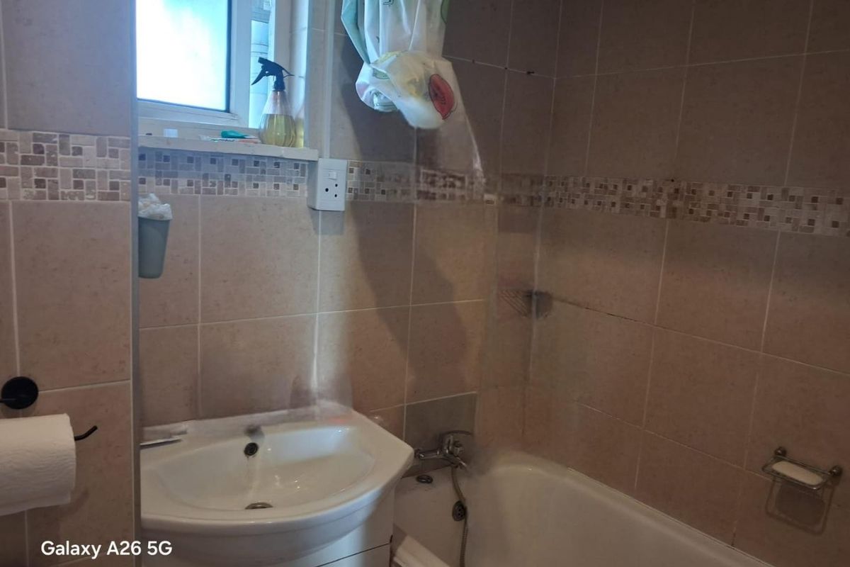 A functional bathroom featuring a bathtub with shower attachment, vanity basin, and neutral wall tiling.