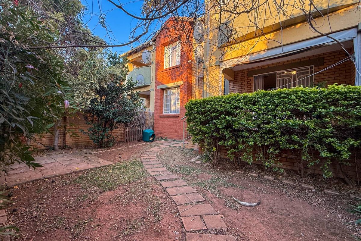 A rear garden area featuring a brick facade, paved walkway, and established hedging, providing a private outdoor space for the apartment.