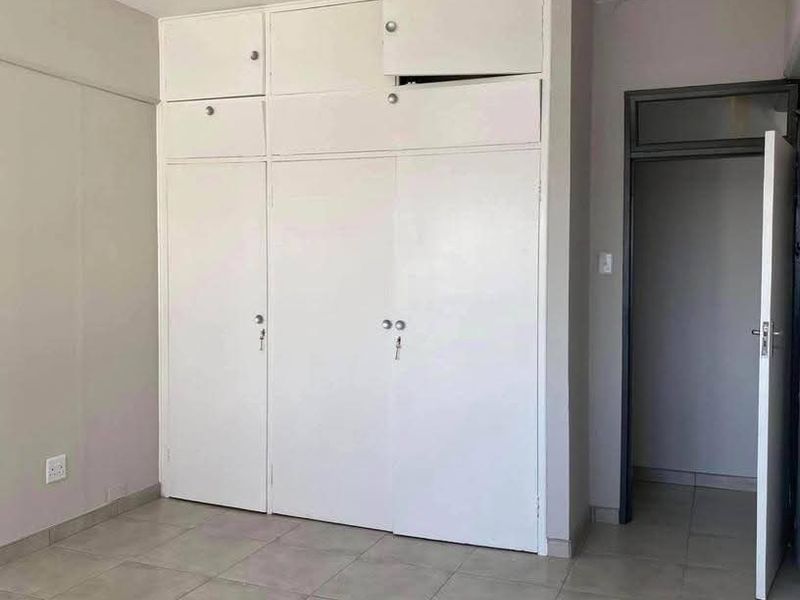 A vacant bedroom featuring neutral tiled flooring and white built-in cupboards with overhead storage compartments.