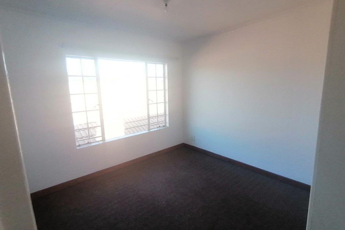 A vacant, neutrally painted bedroom featuring carpeted flooring and a large grid-pattern window allowing for natural light.