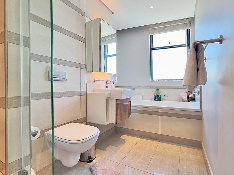 Modern bathroom featuring a wall-mounted toilet, glass shower enclosure, built-in bathtub, and a sleek vanity with a mirrored medicine cabinet.