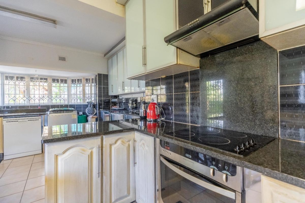 A functional kitchen featuring granite countertops, built-in oven, electric hob, extractor fan, and ample cabinetry, with tiled flooring and natural light from large windows.