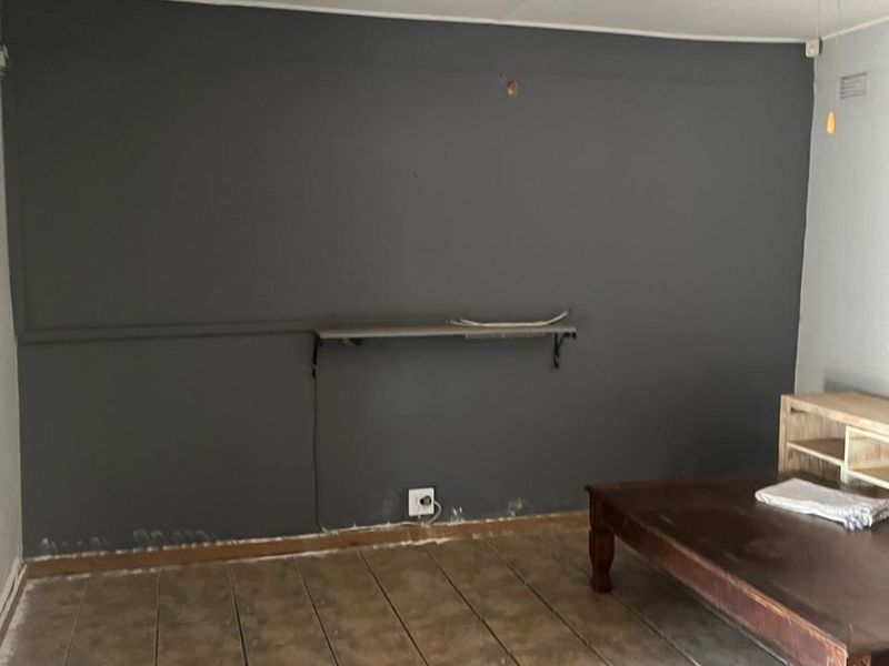 A sparsely furnished living area featuring dark grey accent wall, tiled flooring, and a ceiling fan, requiring cosmetic updates to wall finishes.