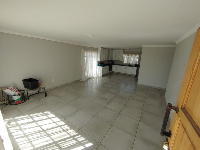 Spacious open-plan living area featuring neutral tiled flooring and a functional kitchen with built-in cabinetry, offering a bright and versatile layout.