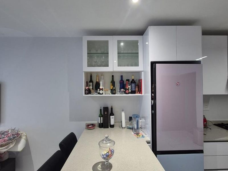 Modern kitchen featuring a long quartz breakfast bar, white cabinetry with glass-front display units, and sleek tiled flooring.