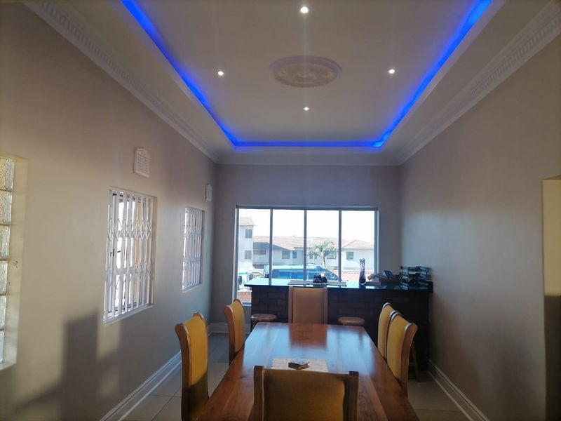 Dining room featuring a built-in brick bar, recessed ceiling with ambient blue LED lighting, and security-fitted windows.