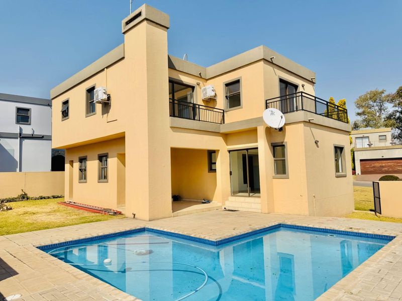 Rear view of a two-story house featuring a swimming pool, paved patio area, balcony, and exterior chimney.