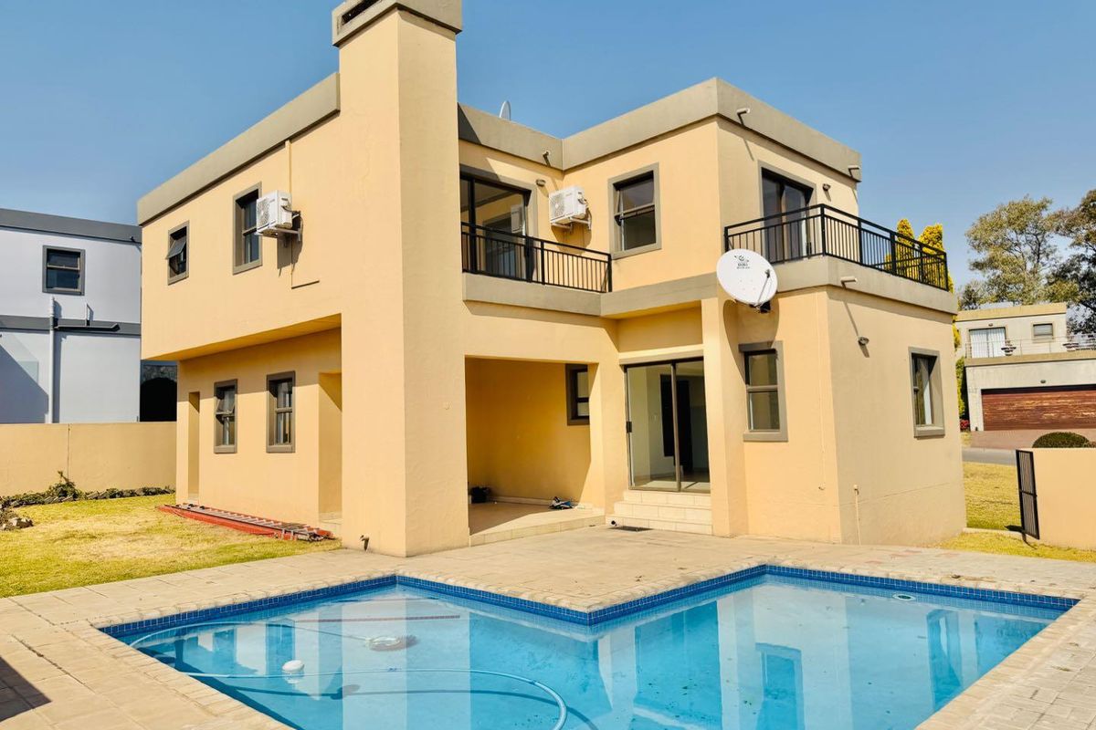 Rear view of a two-story house featuring a swimming pool, paved patio area, balcony, and exterior chimney.