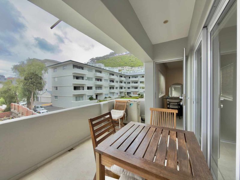 A covered balcony featuring tiled flooring and sliding glass door access, offering an outdoor seating area with views of the surrounding apartment complex.