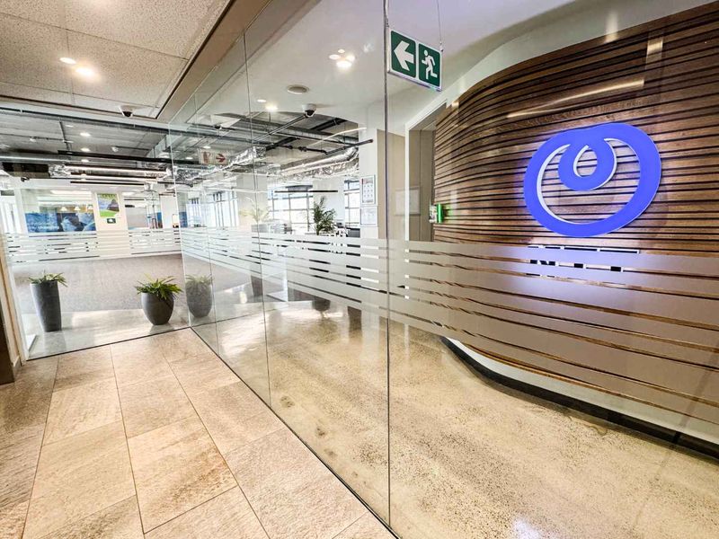 Modern office entrance featuring a glass partition wall, polished stone flooring, and a decorative slatted timber wall with corporate branding.