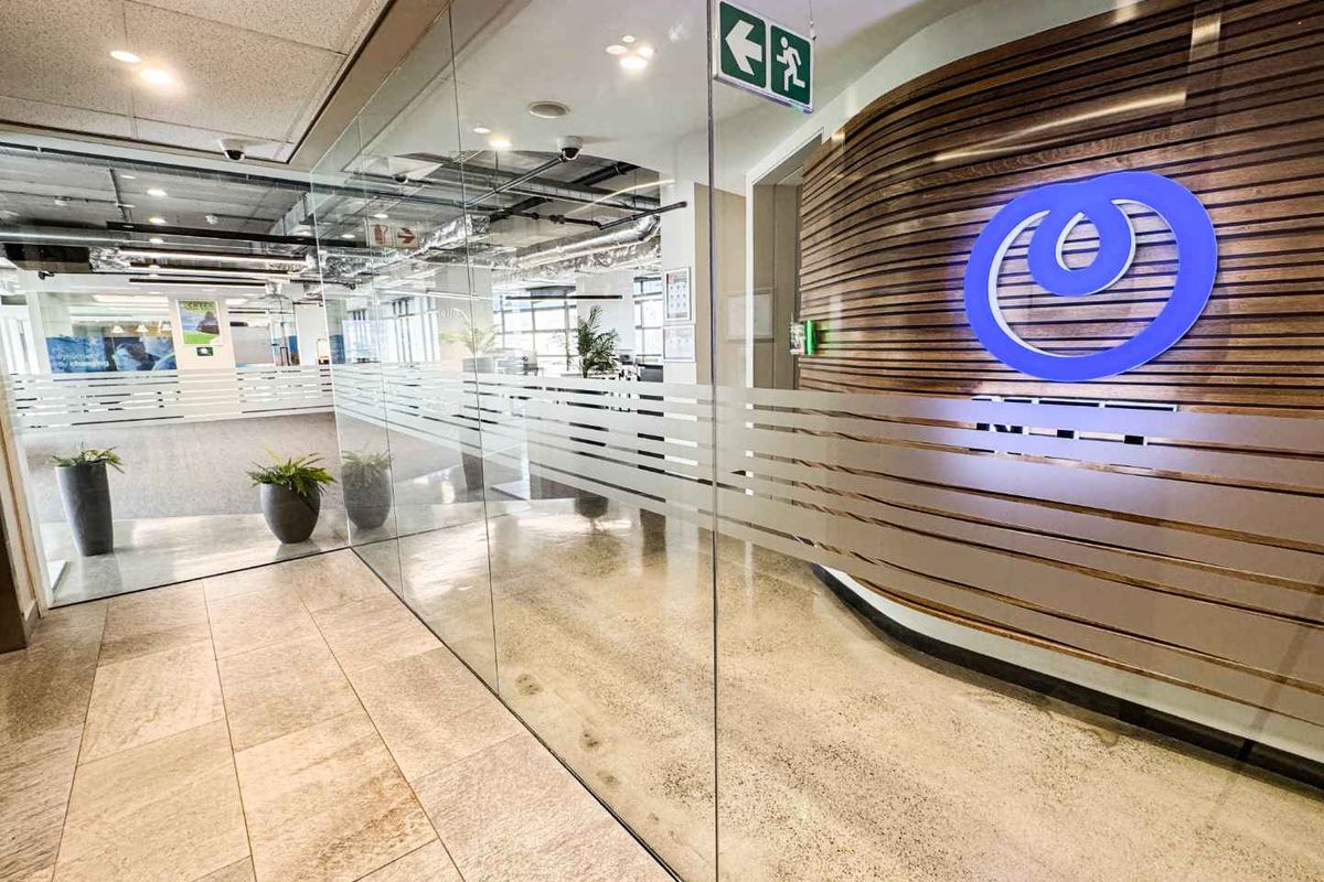 Modern office entrance featuring a glass partition wall, polished stone flooring, and a decorative slatted timber wall with corporate branding.