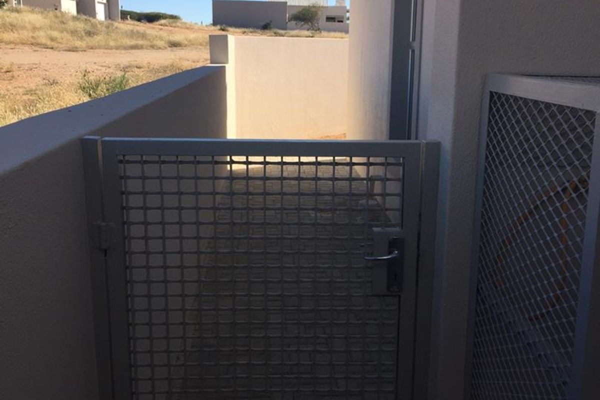 A side access path featuring a secure metal gate and exterior wall-mounted lighting, providing functional outdoor circulation space.