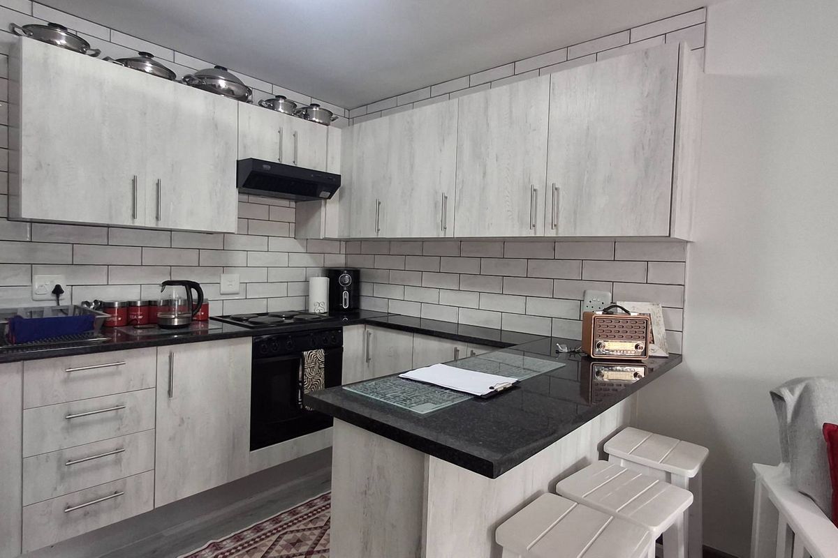 Modern kitchen featuring light wood-grain cabinetry, dark granite countertops, subway tile backsplash, and a functional breakfast bar for casual dining.