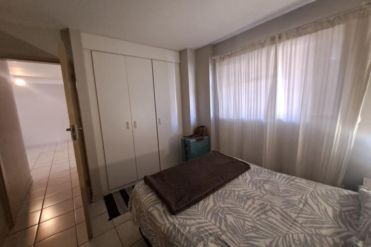 A functional bedroom featuring built-in cupboards, tiled flooring, and natural light through window curtains, offering a clean and simple living space.