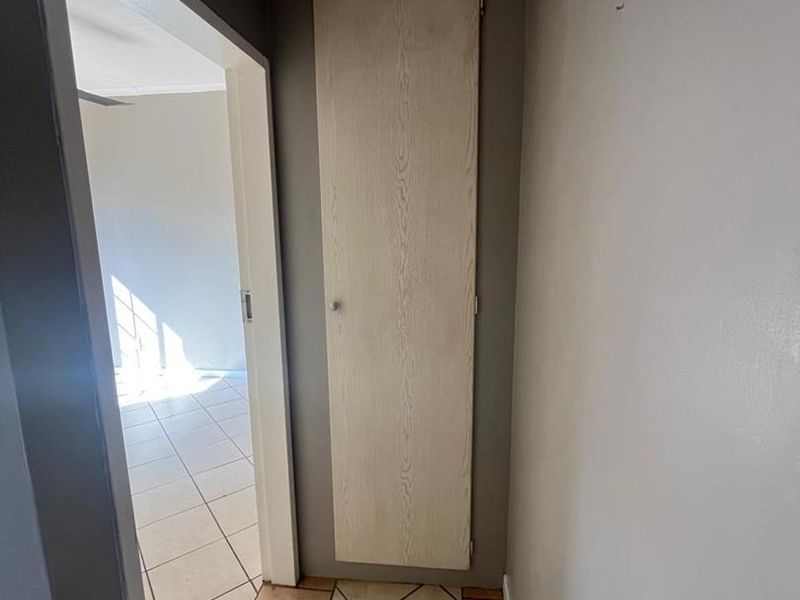 A functional hallway featuring tiled flooring and a built-in storage cupboard, providing access to adjacent rooms.