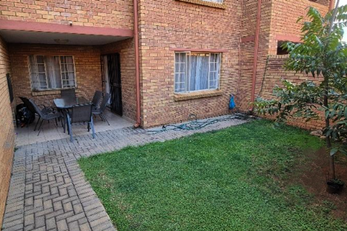 A private rear courtyard featuring a paved patio area, a small lawn, and face brick exterior walls.