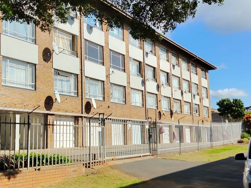 Exterior view of a multi-story apartment building featuring a face brick facade, secure perimeter fencing, and ground-level garage access.