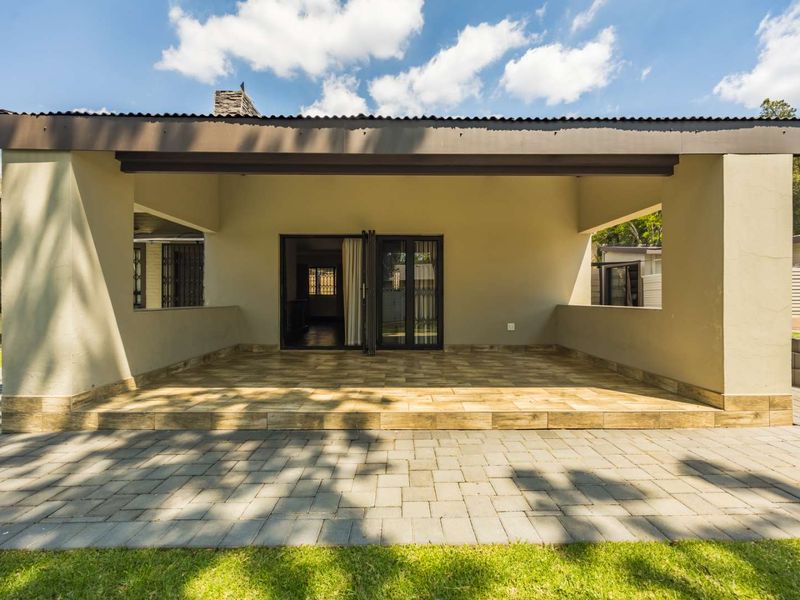 A spacious covered patio featuring tiled flooring and bi-fold doors, leading out to a paved walkway and garden area.