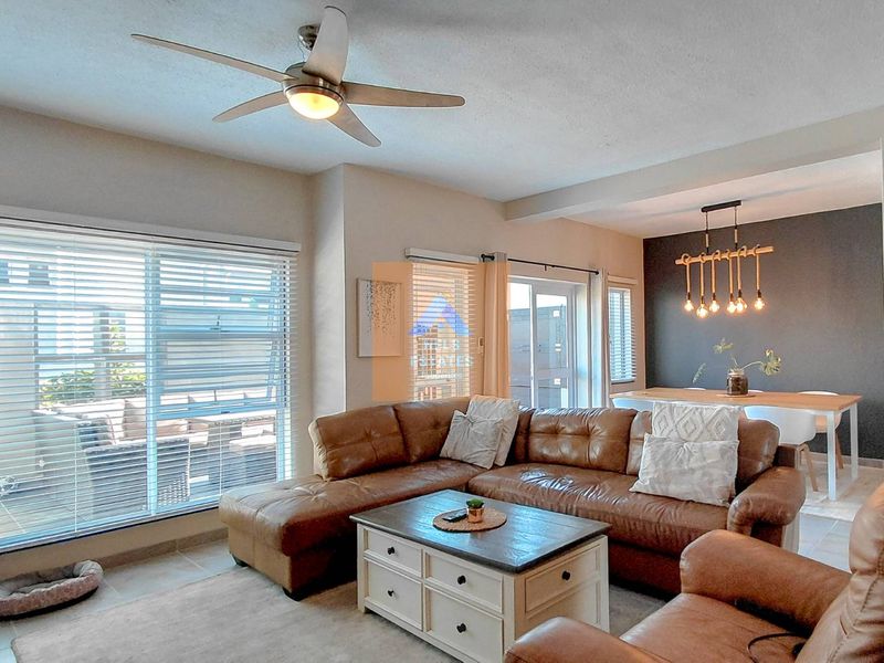 An open-plan living and dining area featuring tiled floors, a ceiling fan, and large sliding glass doors that provide access to the patio.