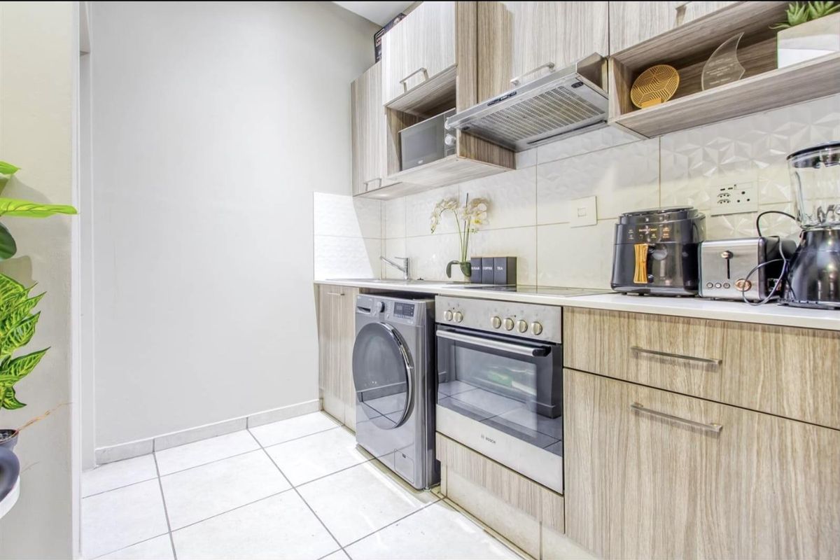 Compact kitchen featuring light wood-grain cabinetry, tiled backsplash, built-in oven with extractor fan, and space for a front-loading washing machine.