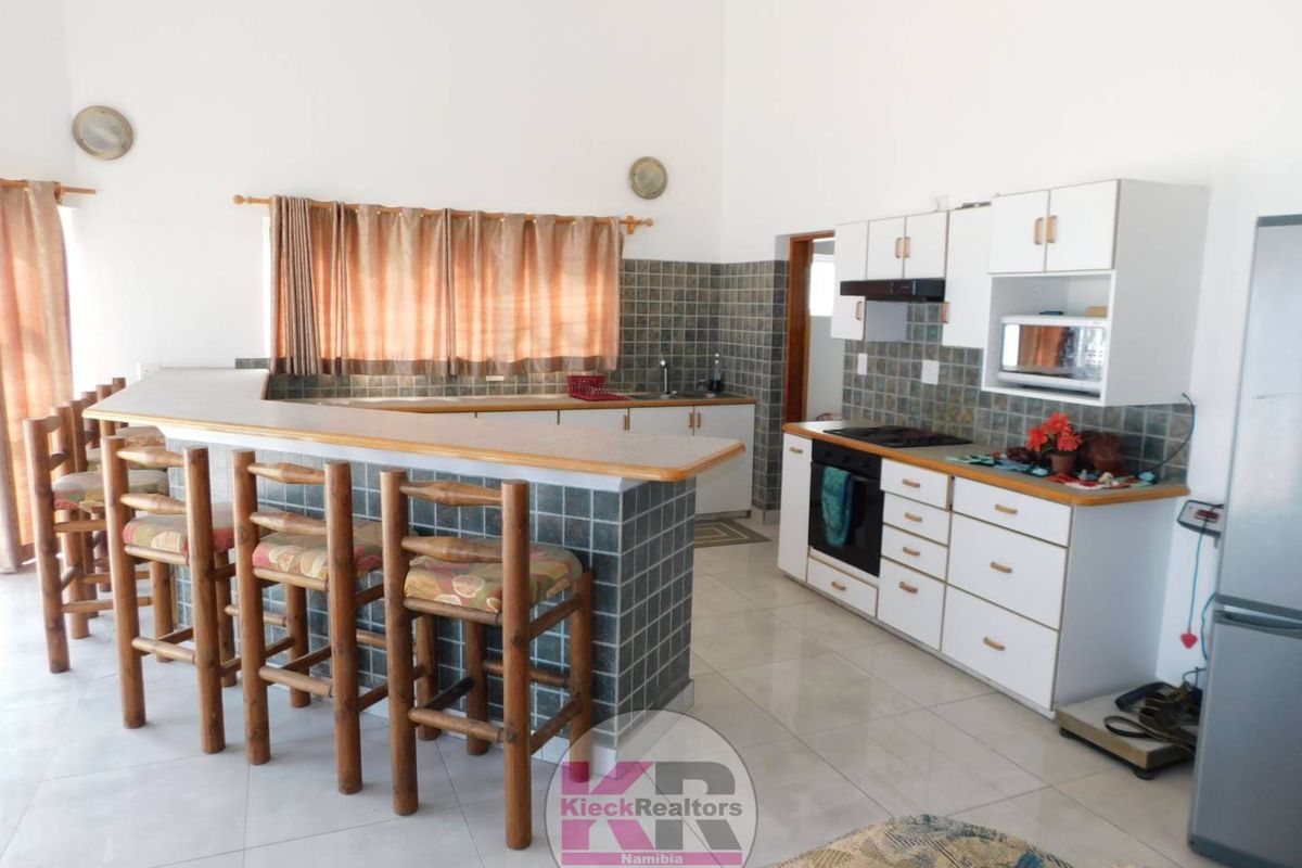 A functional kitchen featuring a tiled breakfast bar, built-in cabinetry, integrated oven and hob, and a tiled backsplash, offering a practical layout.