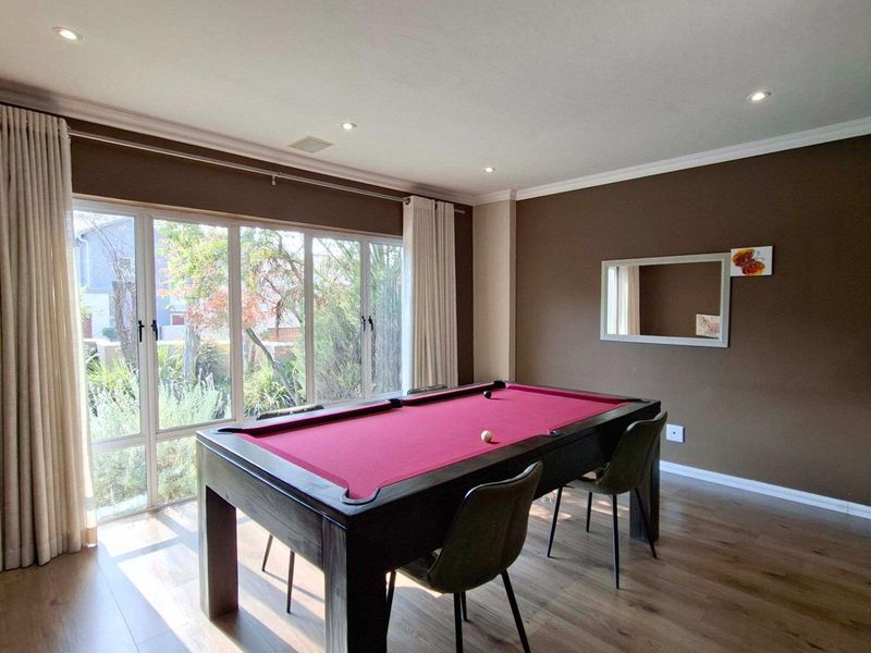 A well-lit living area featuring laminate flooring, recessed downlighting, and large windows that provide ample natural light and a view of the garden.