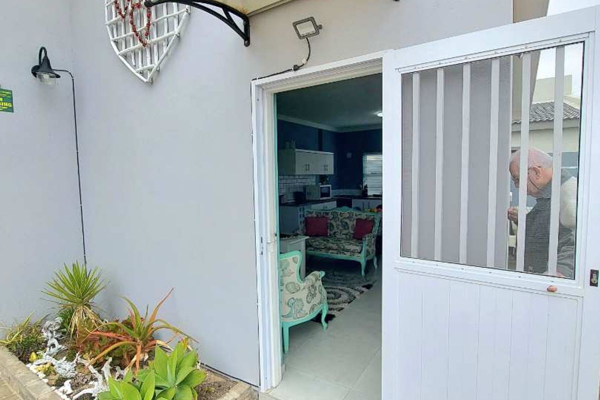 Exterior view of a side entrance featuring a paved walkway, a small built-in garden bed, and a white security door leading into the home.
