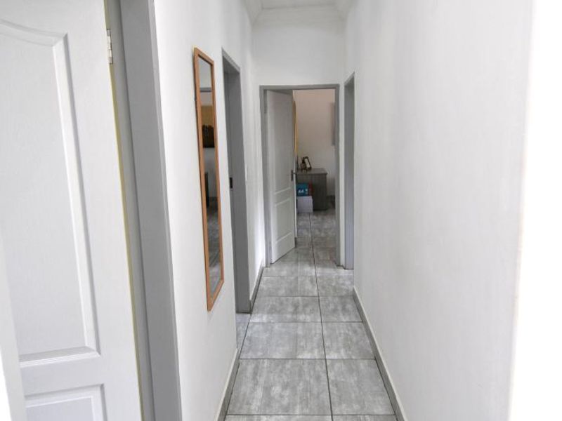 A clean, well-lit hallway featuring modern grey tiled flooring, recessed ceiling downlights, and multiple internal door access points.