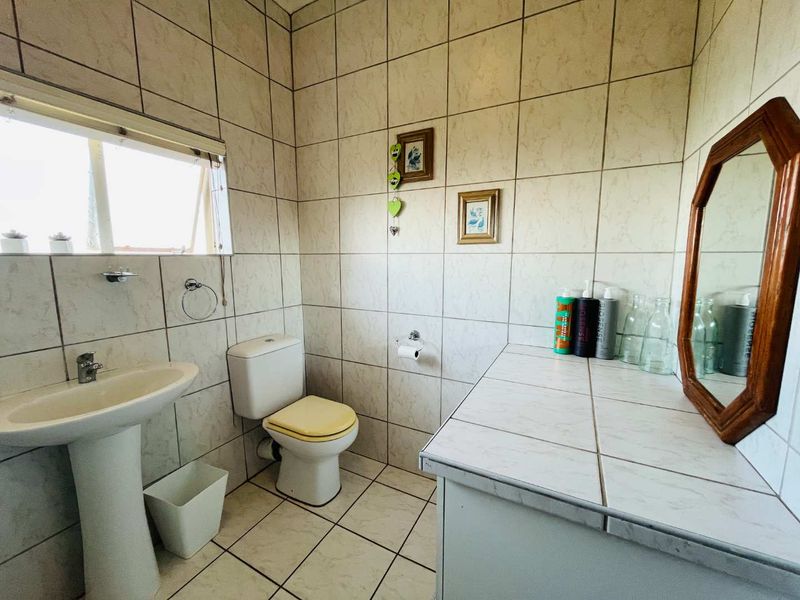 A functional bathroom featuring a pedestal basin, a standard toilet, and a tiled vanity surface with full-height wall tiling.