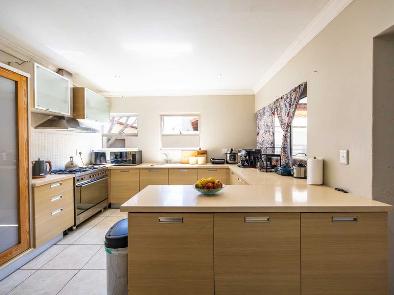 A functional kitchen featuring light wood cabinetry, stone countertops, a gas stove with extractor fan, and tiled flooring.