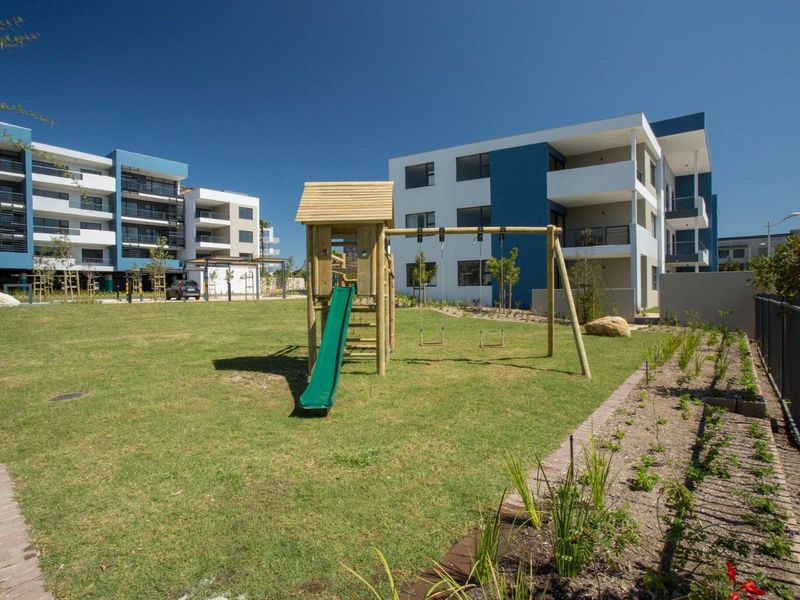 A well-maintained communal garden area featuring a lawn and playground equipment, situated within a modern apartment complex.