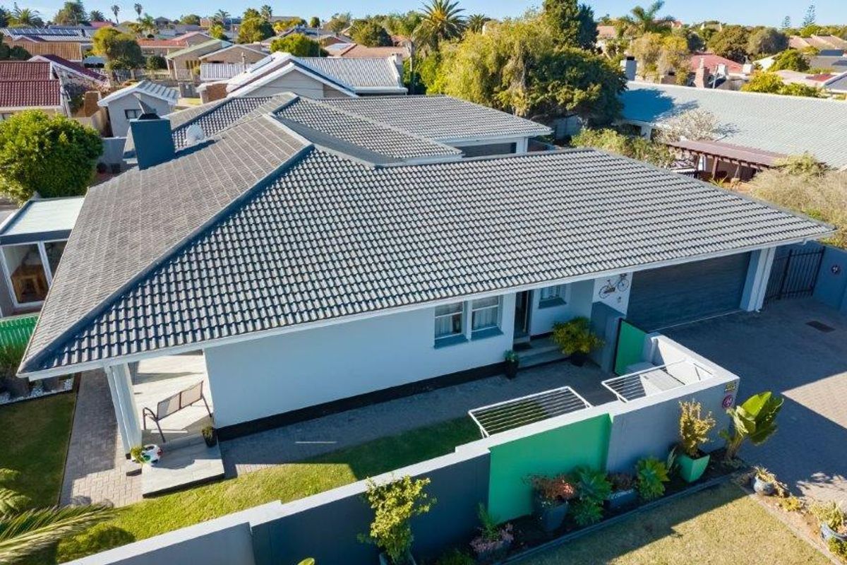 Aerial view of a residential property featuring a tiled roof, paved driveway, boundary wall, and a covered patio area.