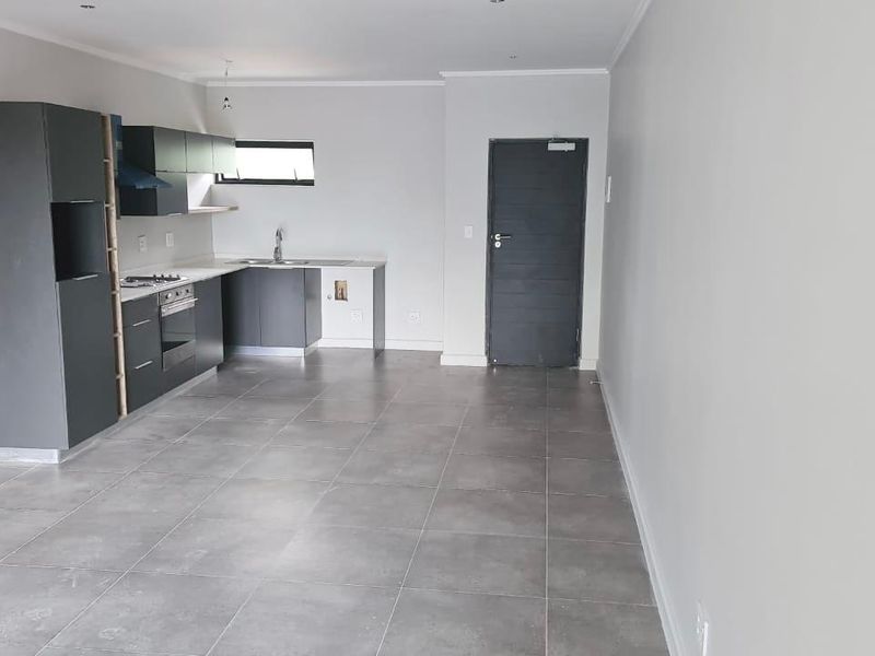 Modern open-plan kitchen featuring dark grey cabinetry, integrated appliances, and neutral tiled flooring in a clean, vacant living space.