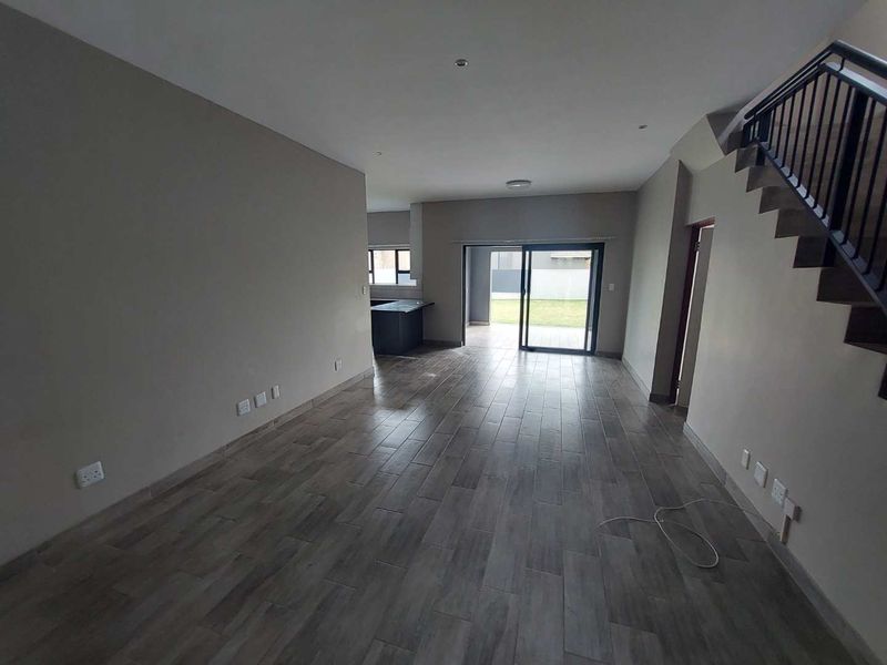 An open-plan living area featuring modern tiled flooring, a staircase with a metal railing, and sliding glass doors leading to the rear garden.