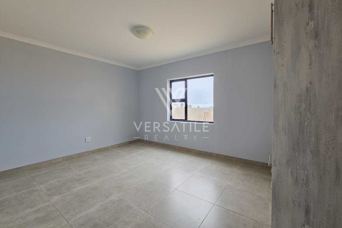 A bright, empty bedroom featuring neutral wall paint, large format floor tiles, and a built-in cupboard.