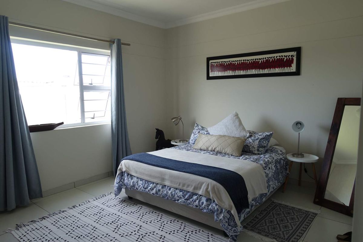 A well-lit bedroom featuring tiled flooring, neutral wall finishes, and a large window providing natural light.