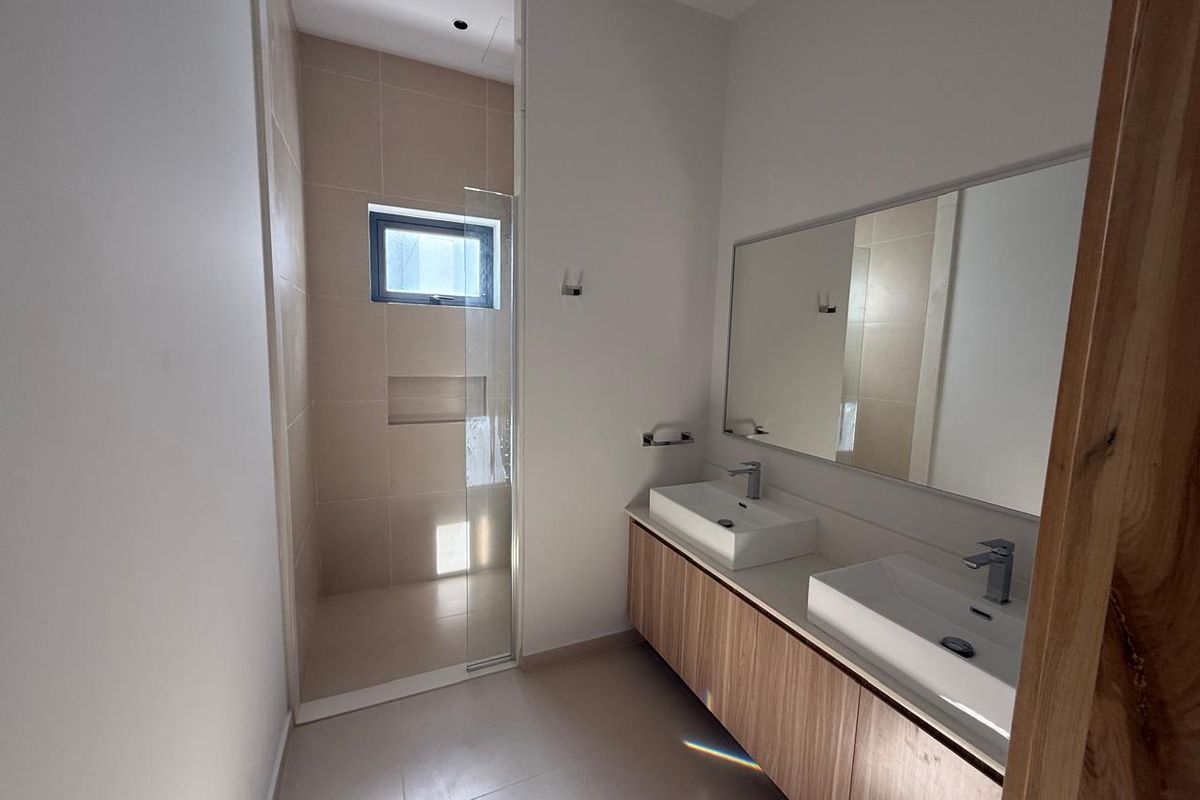Modern bathroom featuring a double vanity with wood-finish cabinetry, large wall-mounted mirror, and a walk-in shower with glass enclosure and tiled niche.