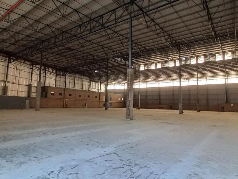 Expansive industrial warehouse space featuring high ceilings with exposed steel trusses, concrete flooring, and an integrated internal office structure.