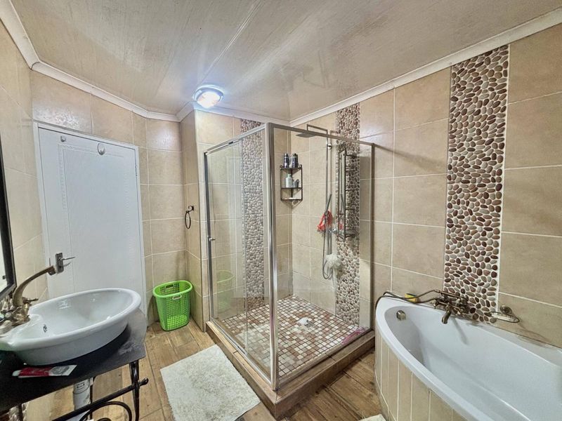 Bathroom featuring a glass shower enclosure, a bathtub, and a vessel sink with decorative pebble tile accents on the walls.