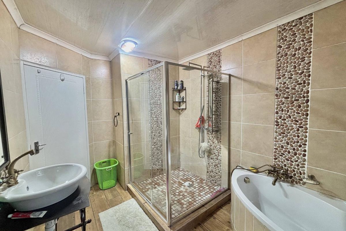 Bathroom featuring a glass shower enclosure, a bathtub, and a vessel sink with decorative pebble tile accents on the walls.