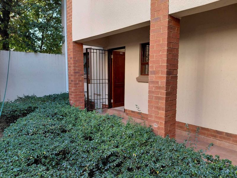 A ground floor entrance featuring a covered patio area with brick pillars, a security gate, and a timber front door.