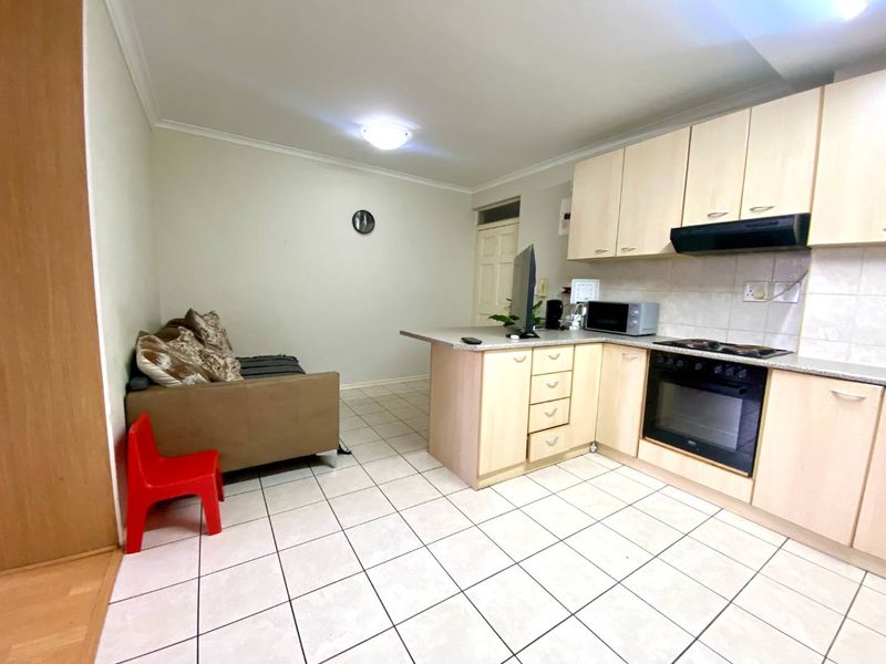 Open-plan kitchen and living area featuring light wood-finish cabinetry, built-in oven and hob, and neutral tiled flooring throughout.
