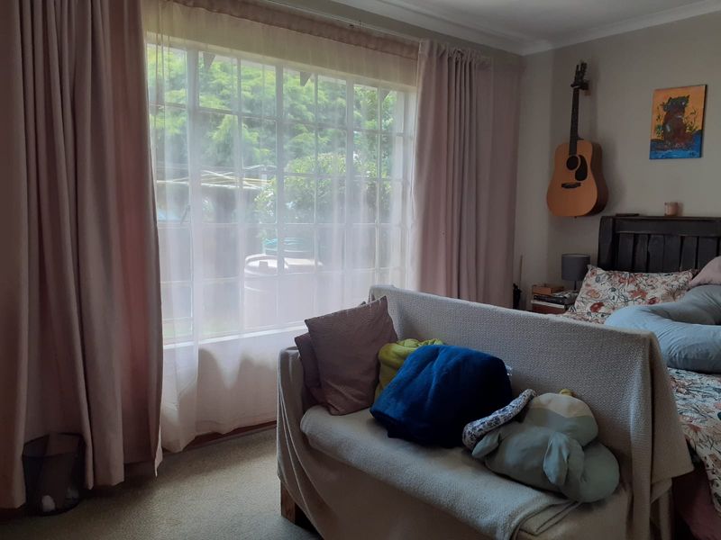 A bedroom featuring a large window with natural light, carpeted flooring, and neutral wall tones.