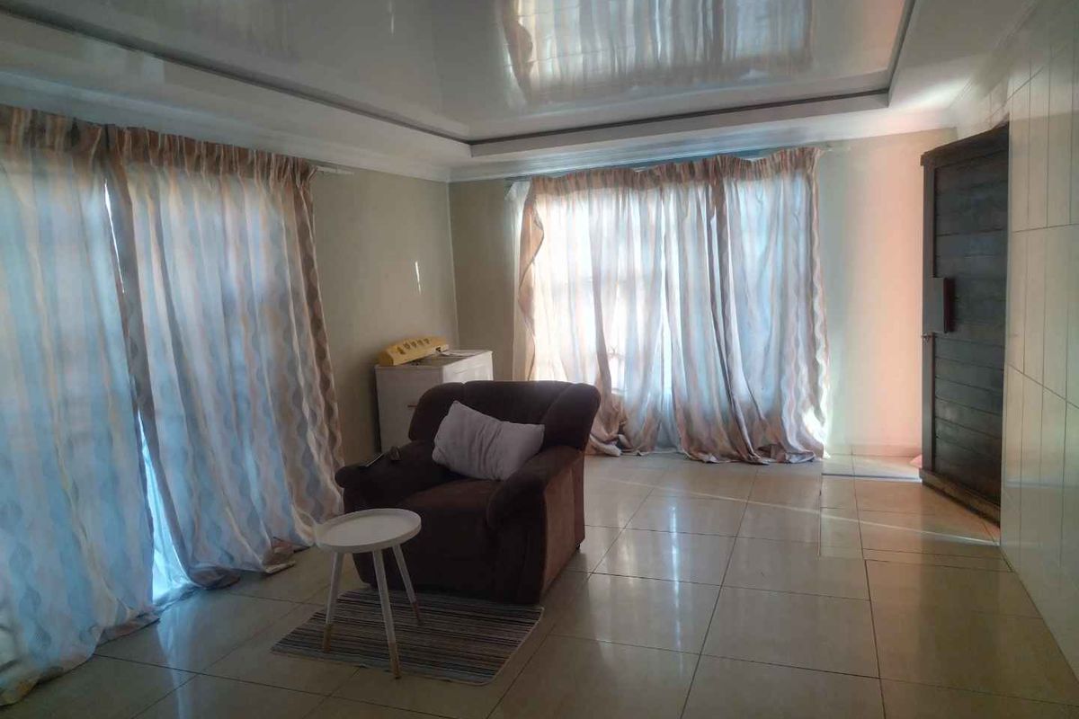 A spacious living area featuring large windows with curtains, tiled flooring, and a glossy ceiling finish.