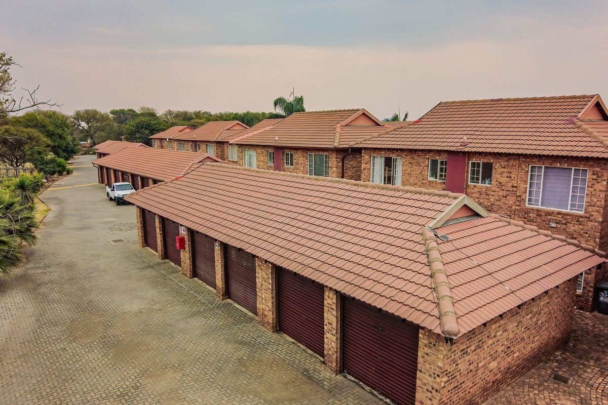 Aerial view of a townhouse complex featuring multiple garage units, brick exterior walls, and tiled roofing with a paved driveway.