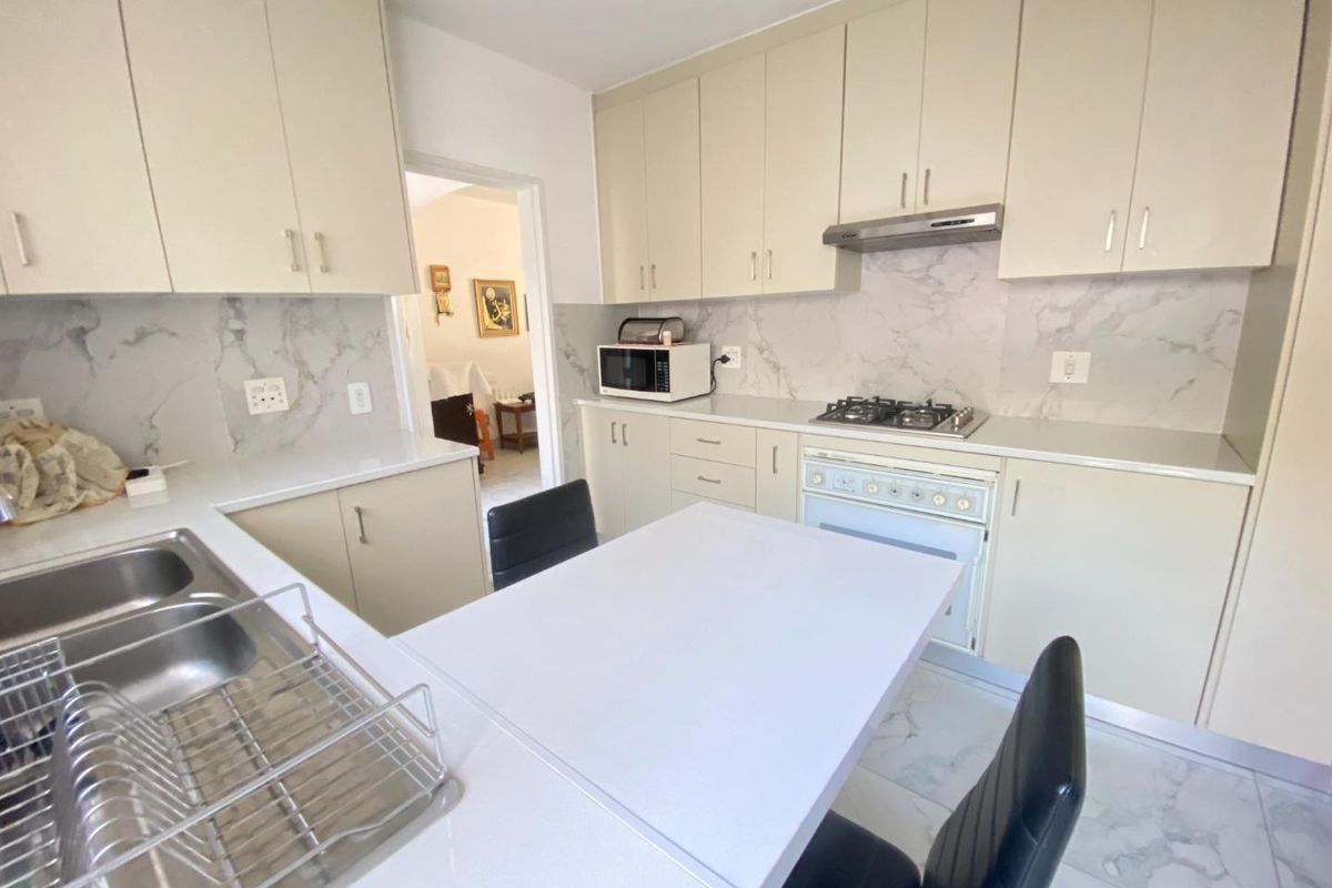 A functional kitchen featuring light-toned cabinetry, marble-look splashbacks, a built-in gas hob, oven, and an integrated breakfast counter.