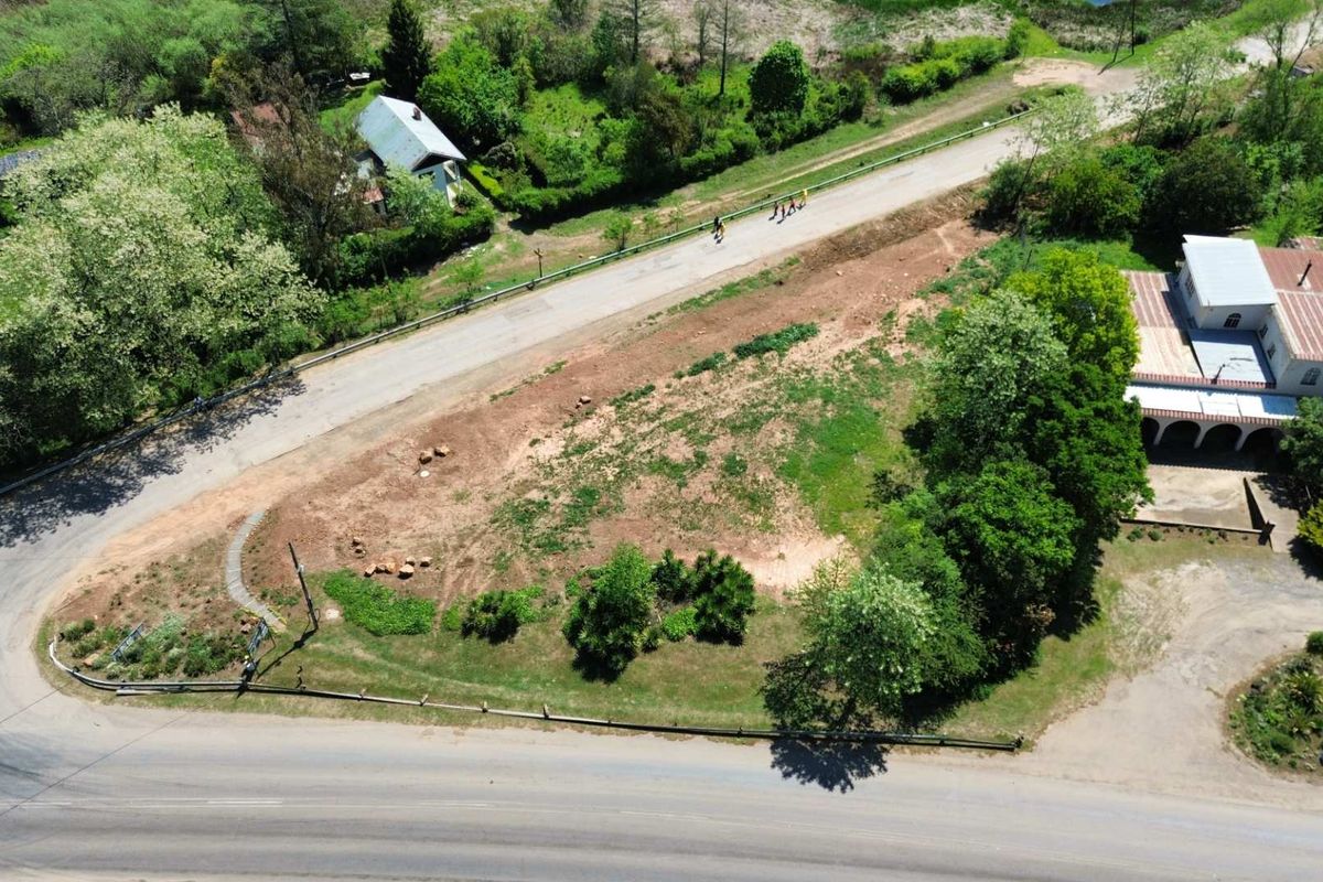 Aerial view of a vacant commercial land plot featuring road access and established greenery, suitable for development.